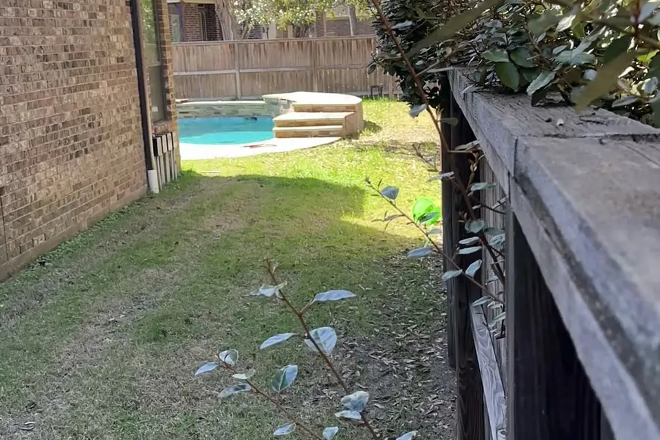 A fenced suburban backyard with a pool seen from the side yard
